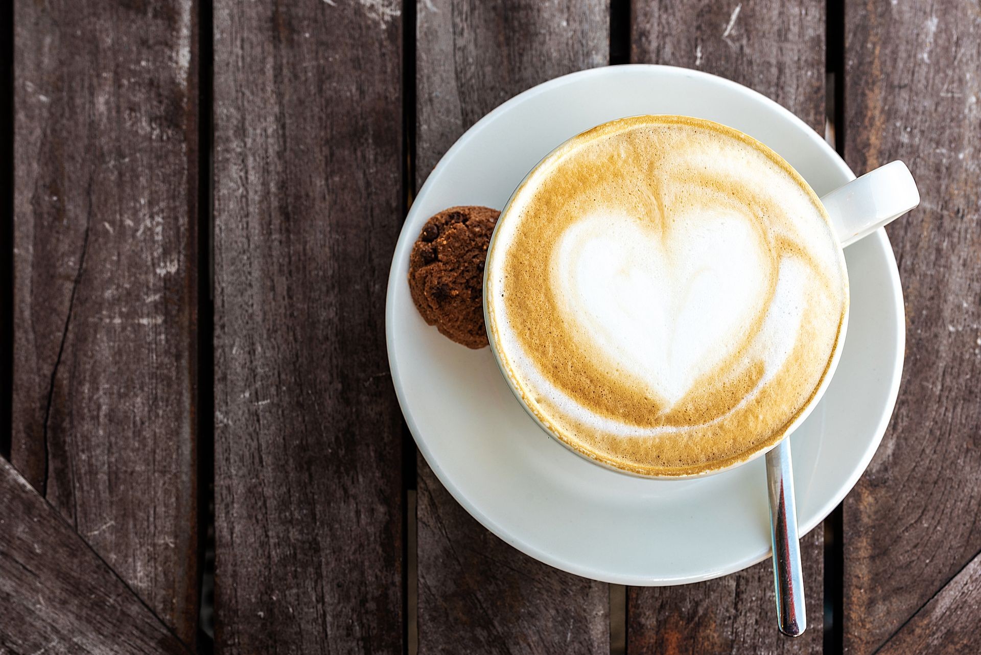 top view of cup of cappuccino with heart shape in milk froth on wooden table